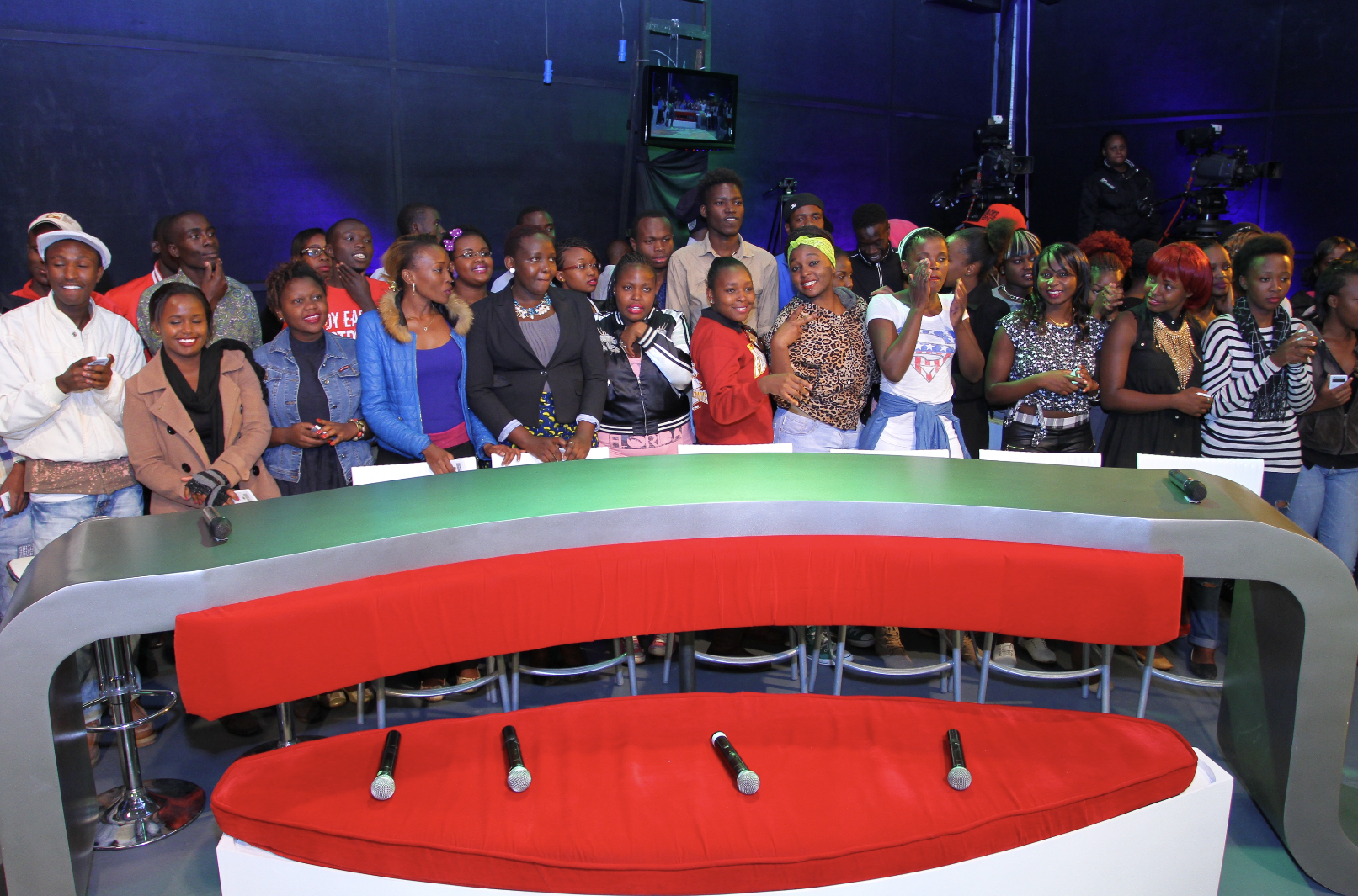 Live studio audience standing behind a red broadcast desk
